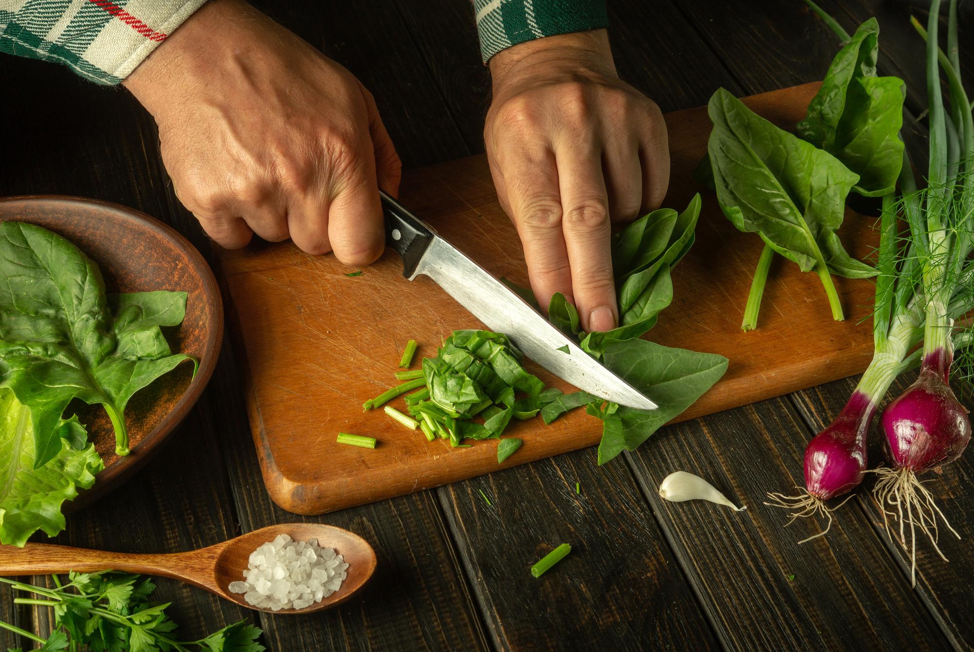 Close-up of hands chopping fresh herbs on wooden board